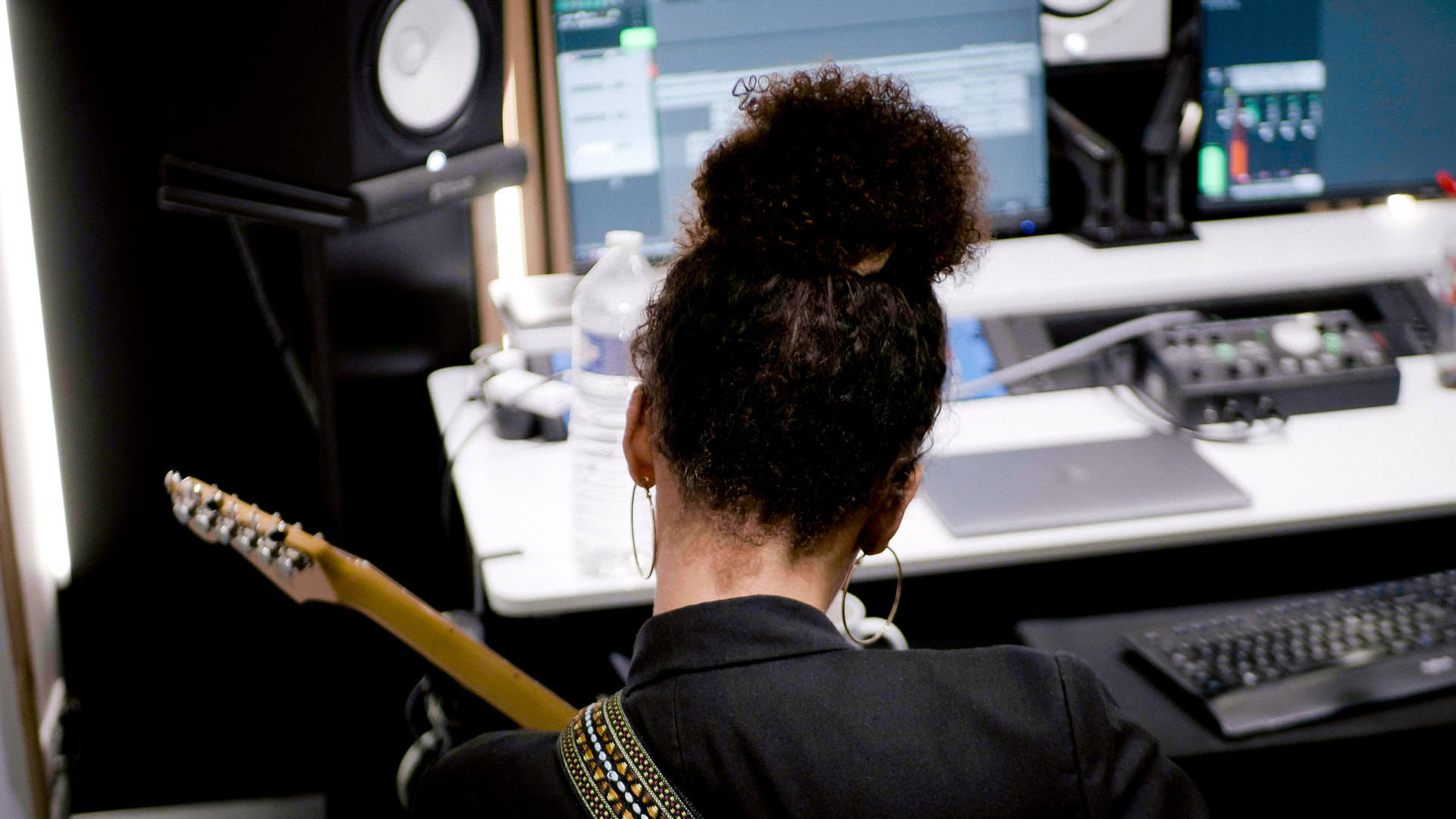 Noeme working at the studio desk with her guitar